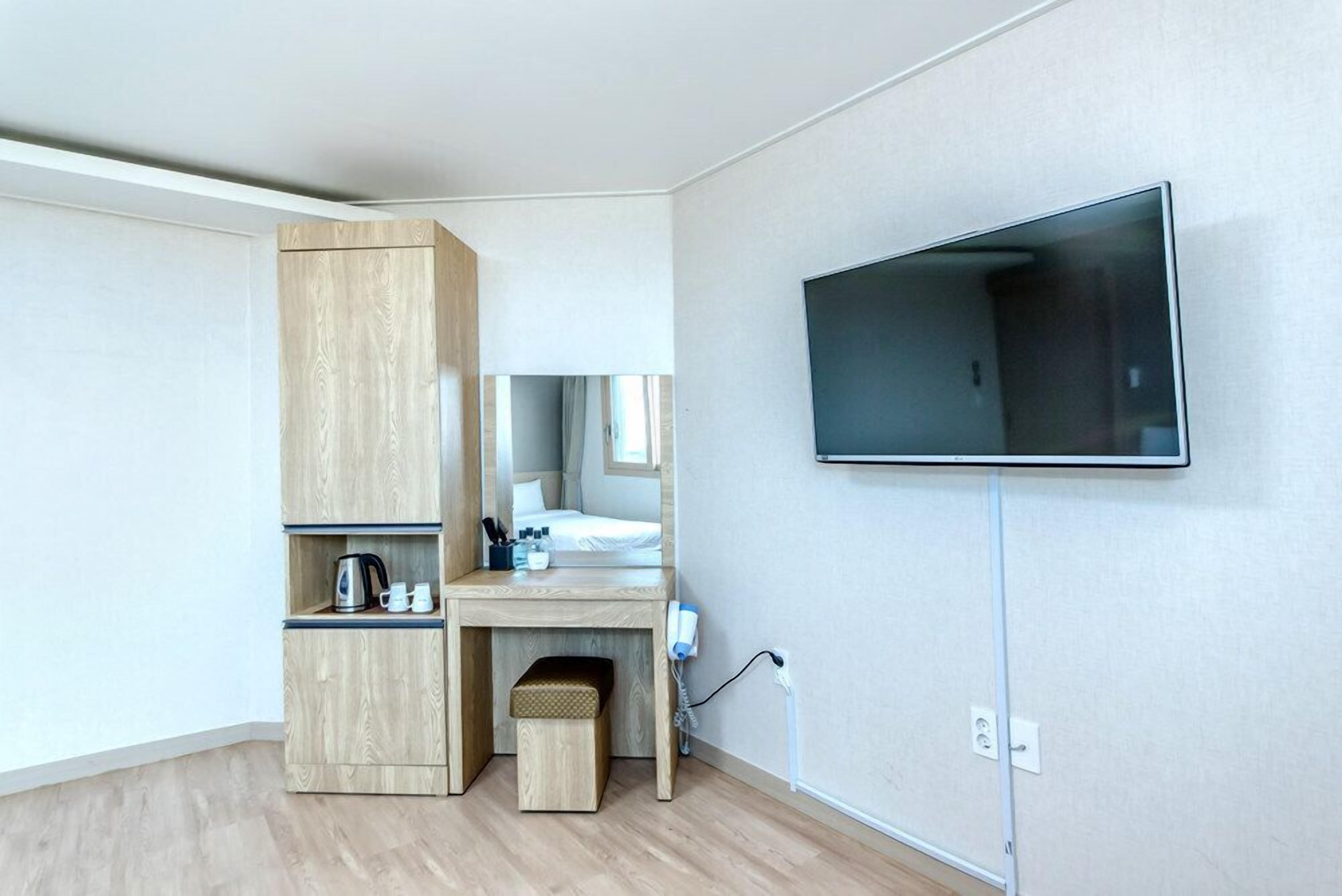 A modern bedroom with a built-in wooden desk, a flat-screen TV mounted on the wall, and a small bedside table.