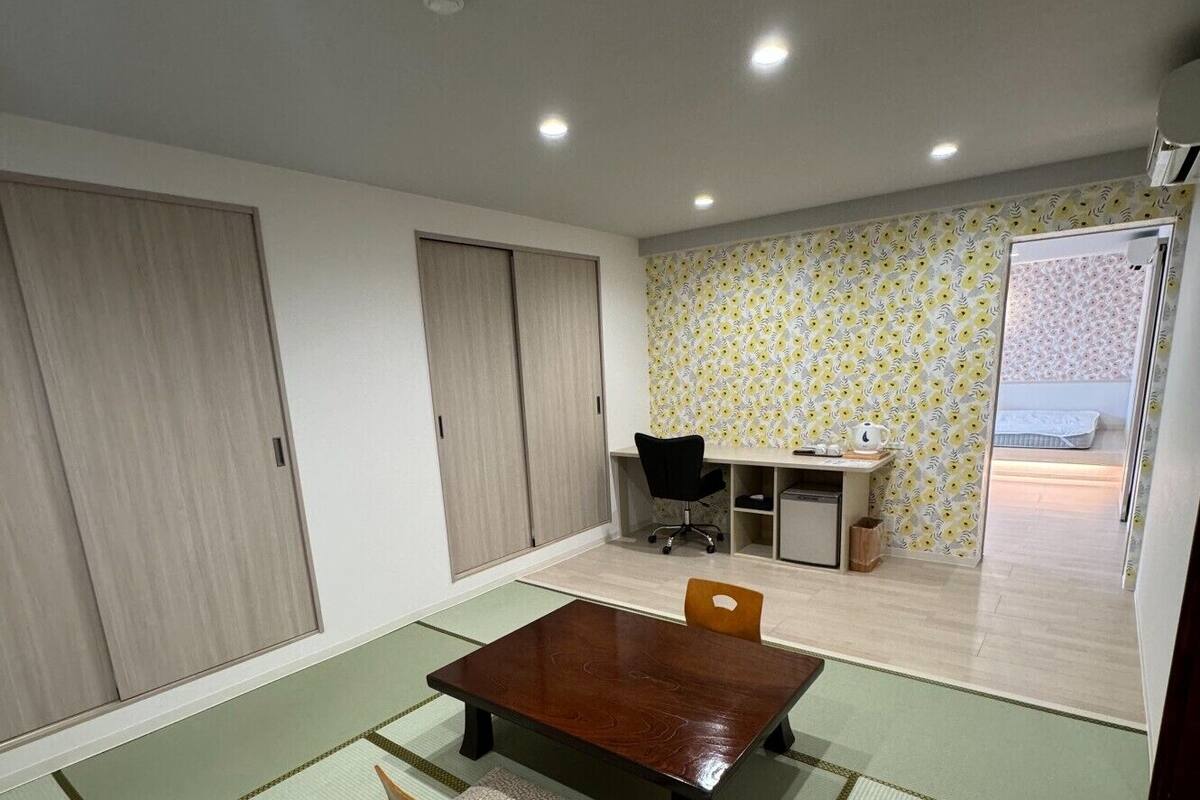 A room with tatami mats, a wooden table, chairs, a desk, and a wardrobe.
