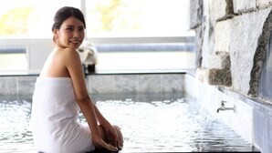 A person sitting in a spa tub with a stone wall and a faucet visible. - Komeyaclub Okutsu (Kagamino)