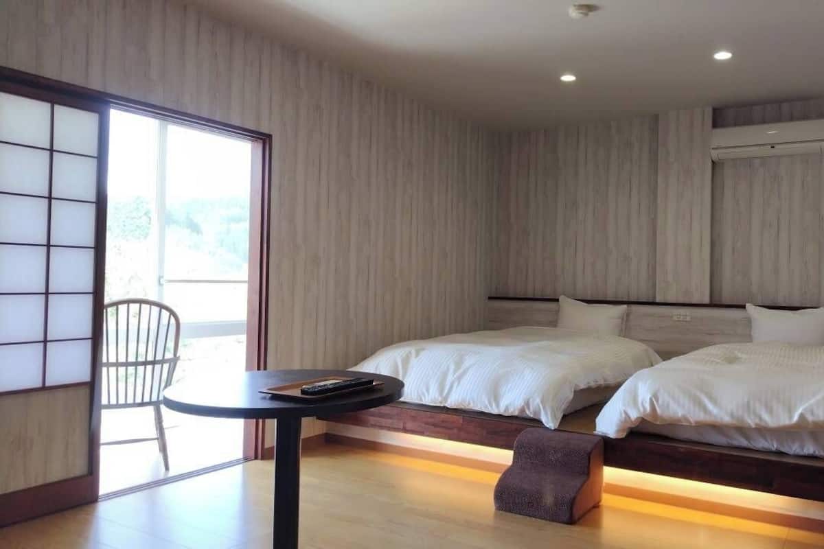 A modern hotel room with two beds, a small table, and a chair.