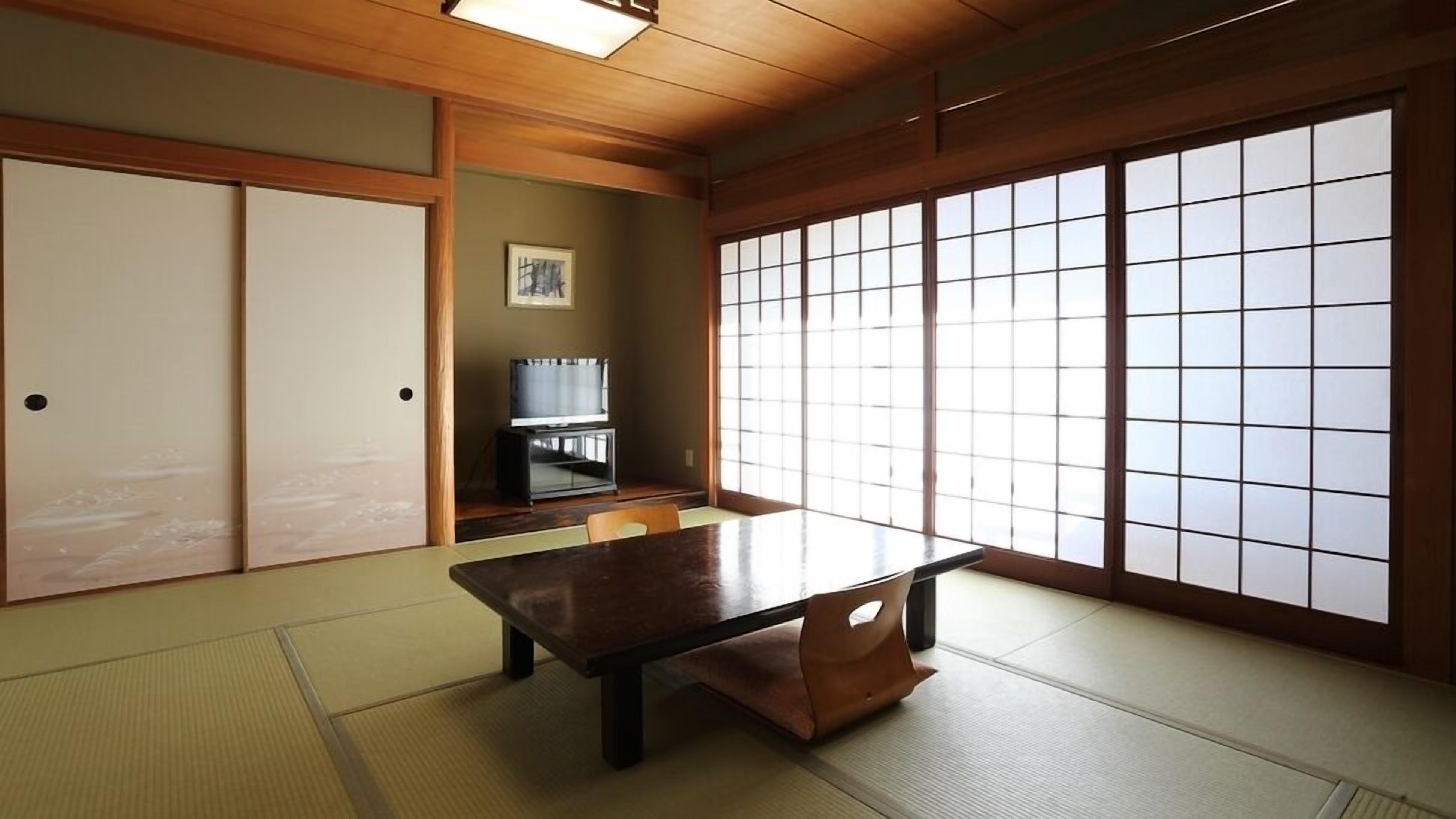 A traditional Japanese room with tatami flooring, a low table, sliding doors, and a large window with shoji screens.
