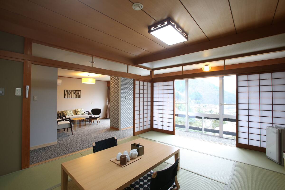 A traditional Japanese room with tatami flooring, a low table with tea sets, sliding shoji doors, and a view of the outdoors.