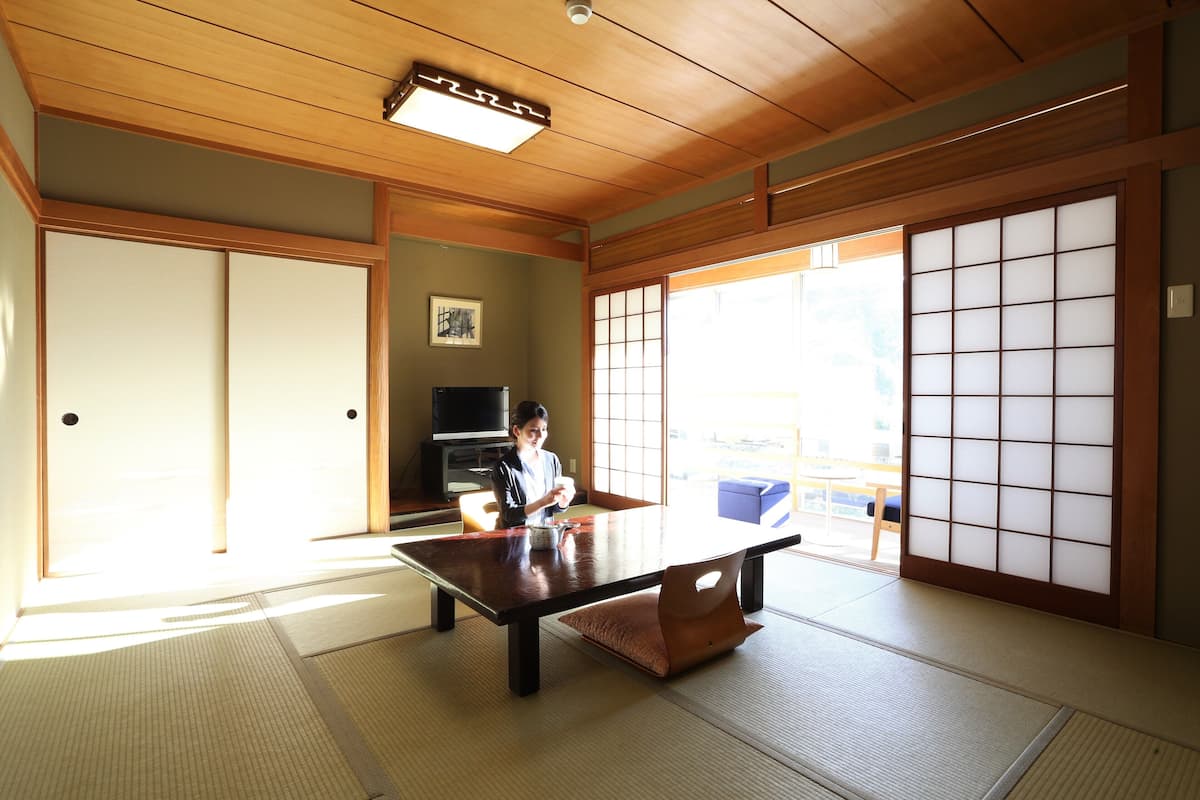A tatami mat room with a low table, sliding doors, and a television in the background.