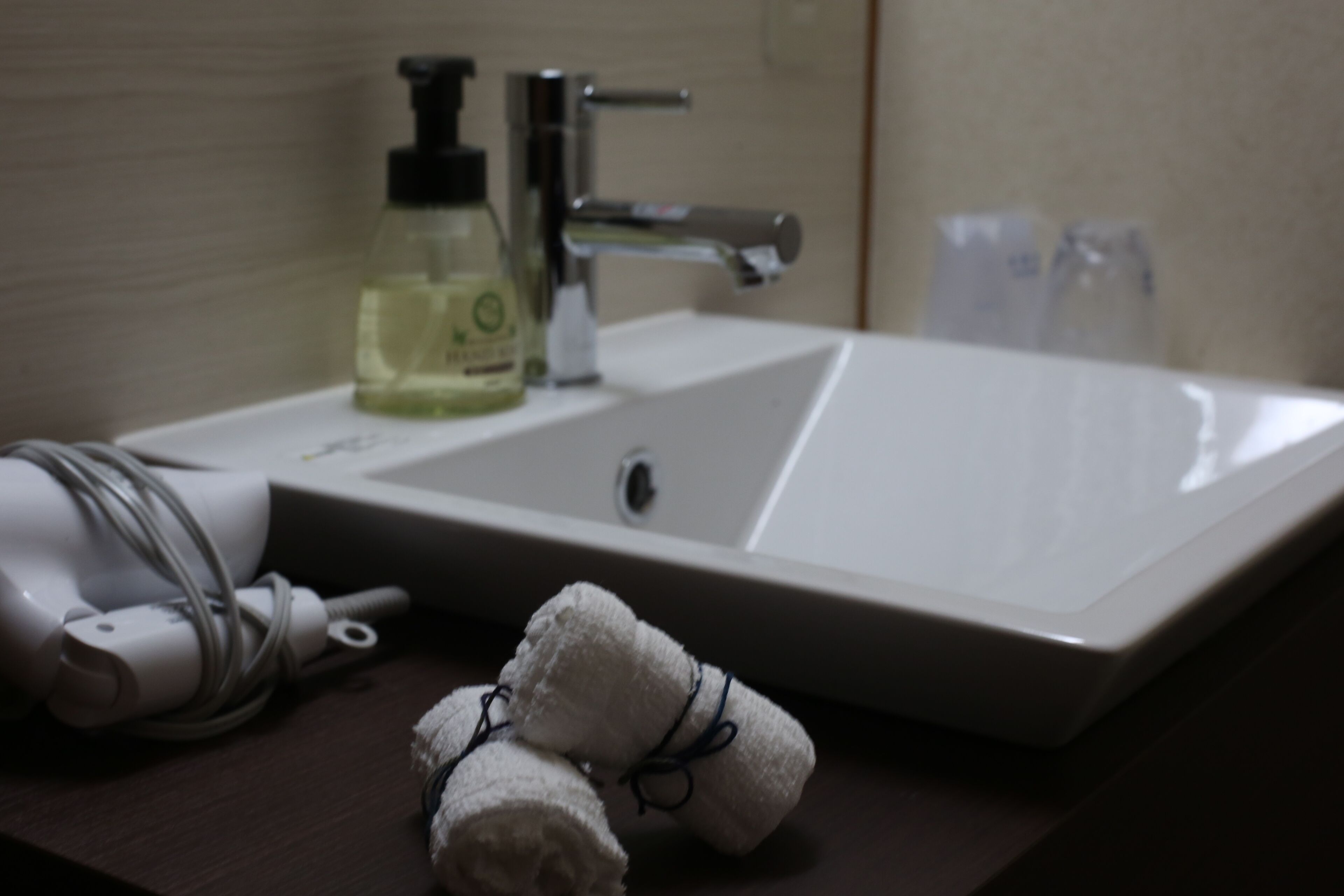A bathroom sink with a bottle of liquid soap, a hairdryer, and a towel on the counter.