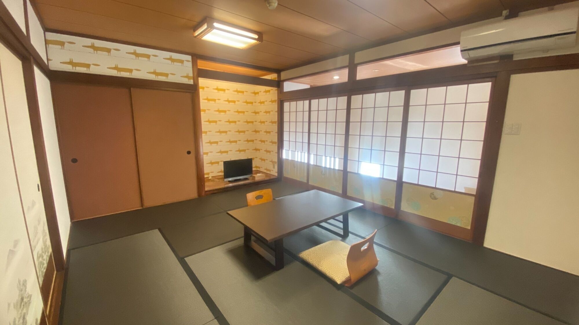 A traditional Japanese room with tatami flooring, a low table, a television, sliding doors, and a view through a shoji screen.