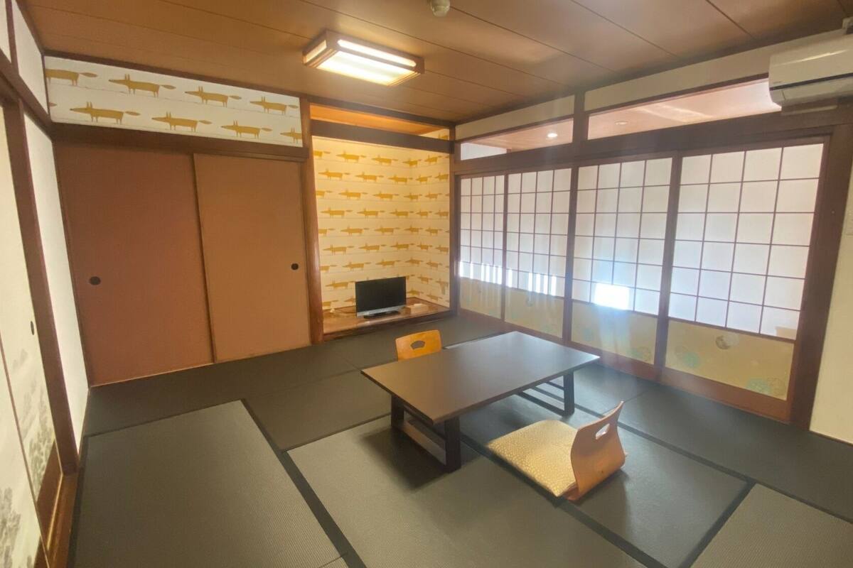 A traditional Japanese room with tatami flooring, a low table, a television, sliding doors, and a view through a shoji screen.