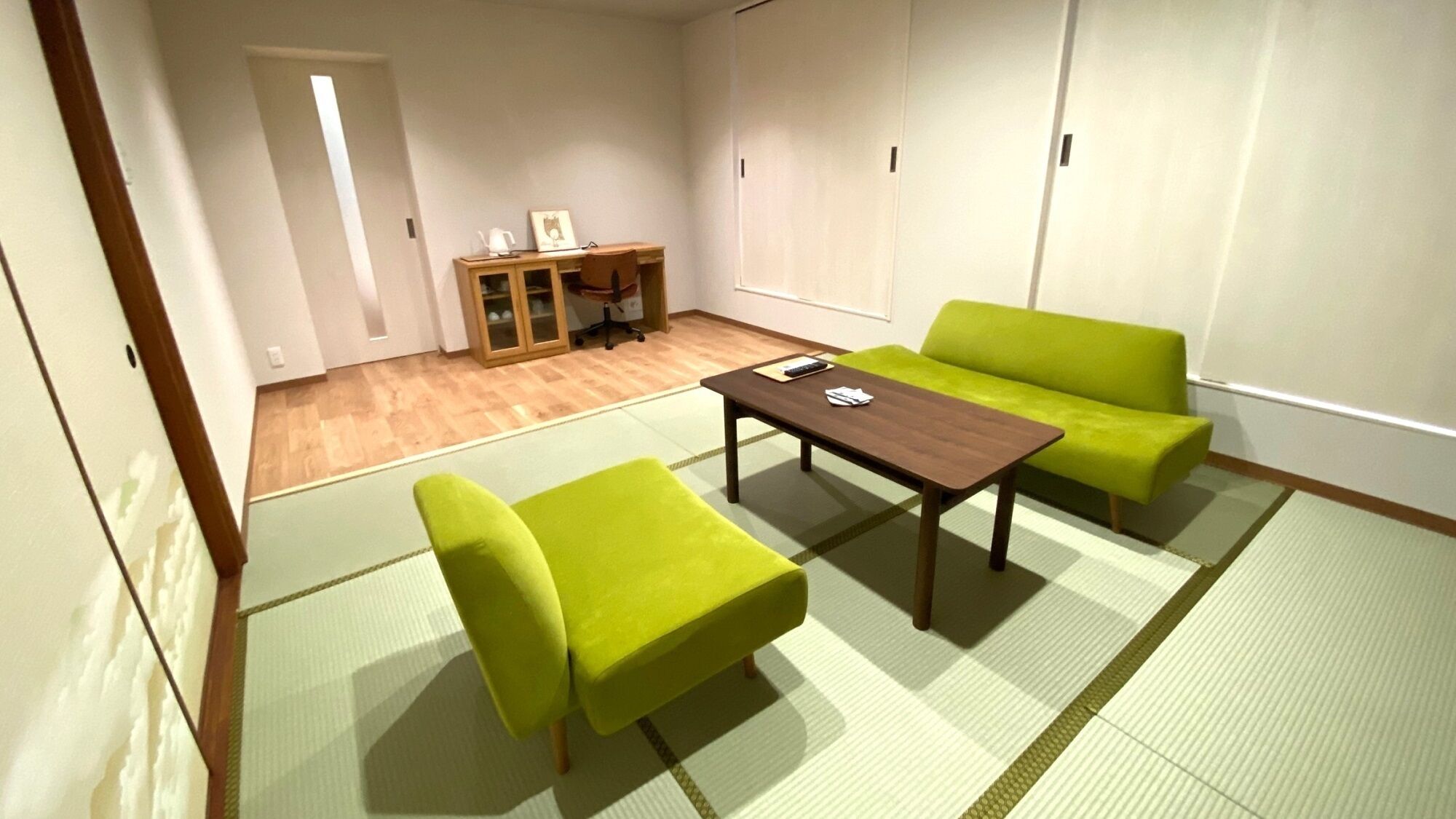 Una habitación con suelo de tatami, una mesa de madera, dos sillas verdes y un sofá.