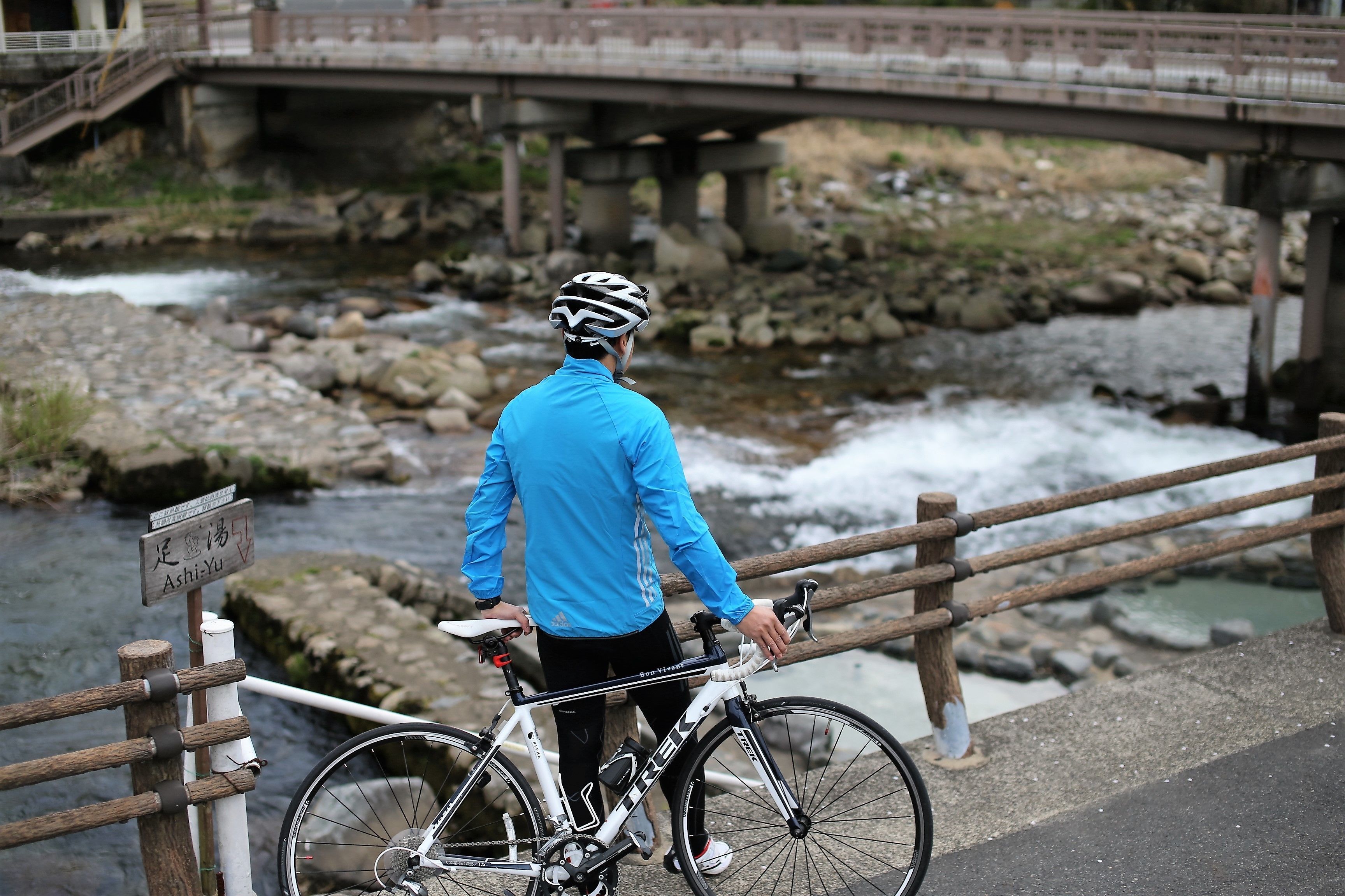 A person standing next to a bicycle on a bridge with a river below.