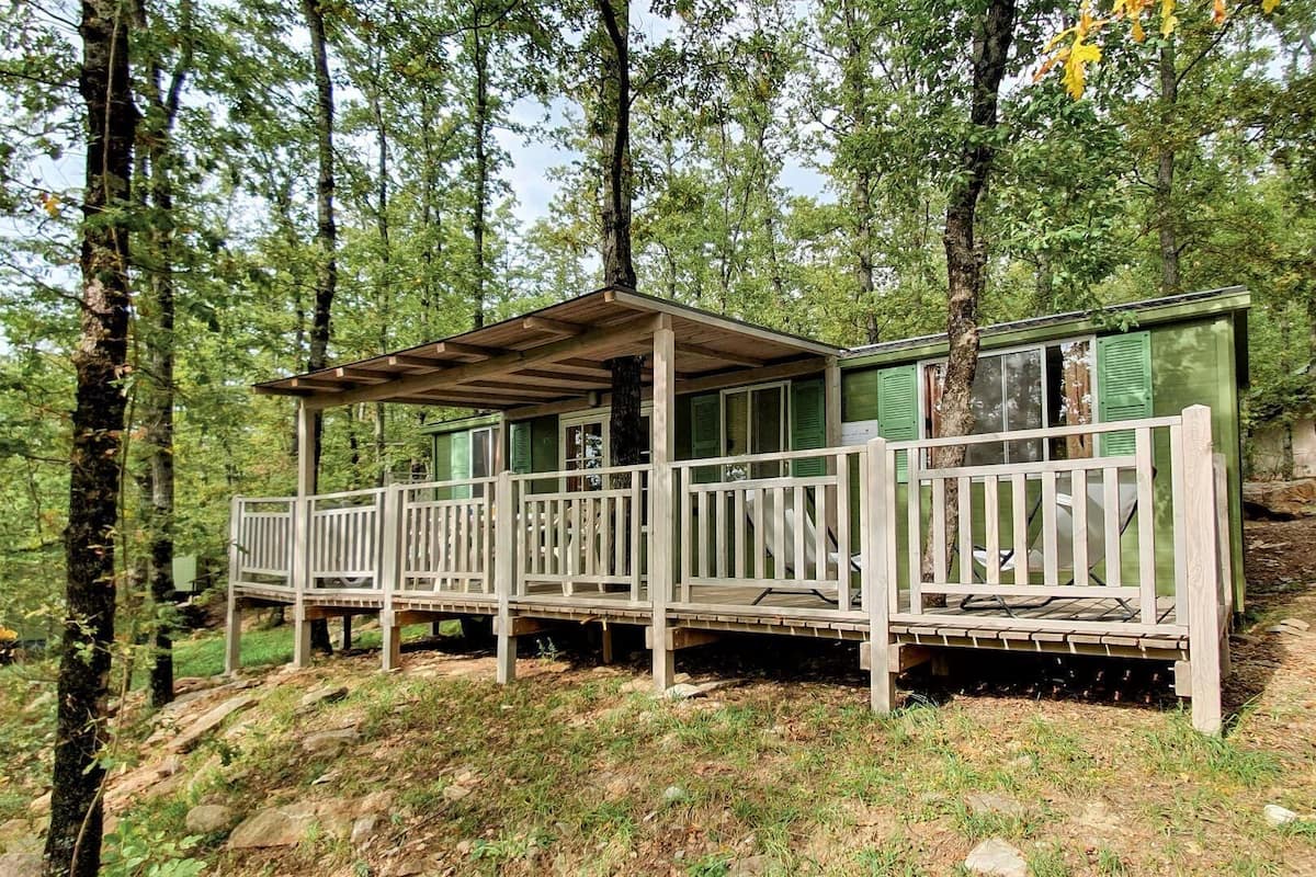 Een houten vakantiehuisje met een veranda, omringd door bomen.