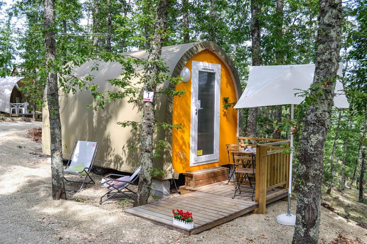 Een klein, vrijstaand huisje met een houten terras, een stoel en een tafel.