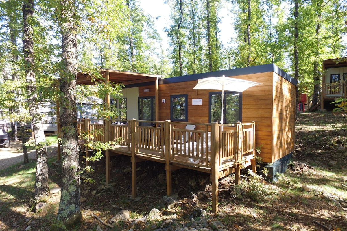 Een houten hutje met een terras, omringd door bomen.