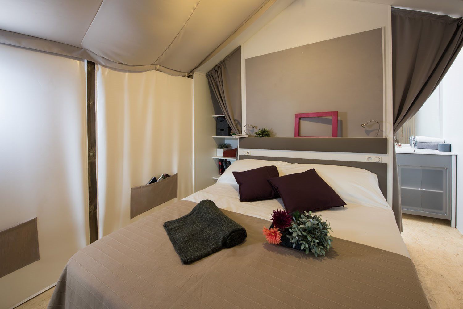 A hotel room with a bed, a bedside table, a mirror, and a window with curtains.
