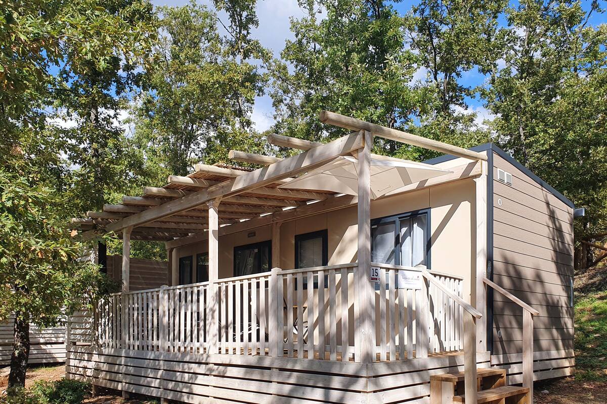 Een houten hut met een overdekte veranda, een trap en een omheind terras.