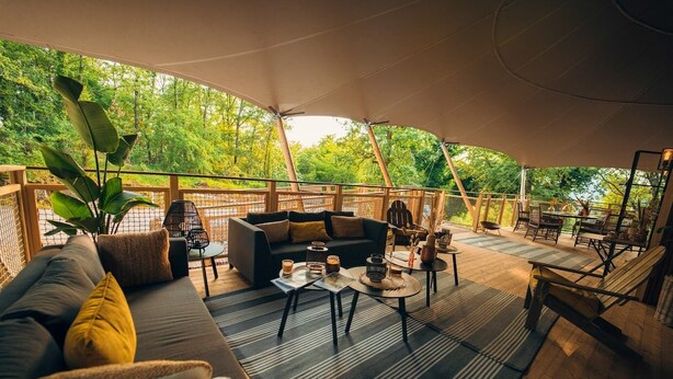 An outdoor seating area with a sofa, tables, and chairs, surrounded by a wooden deck and a canopy.