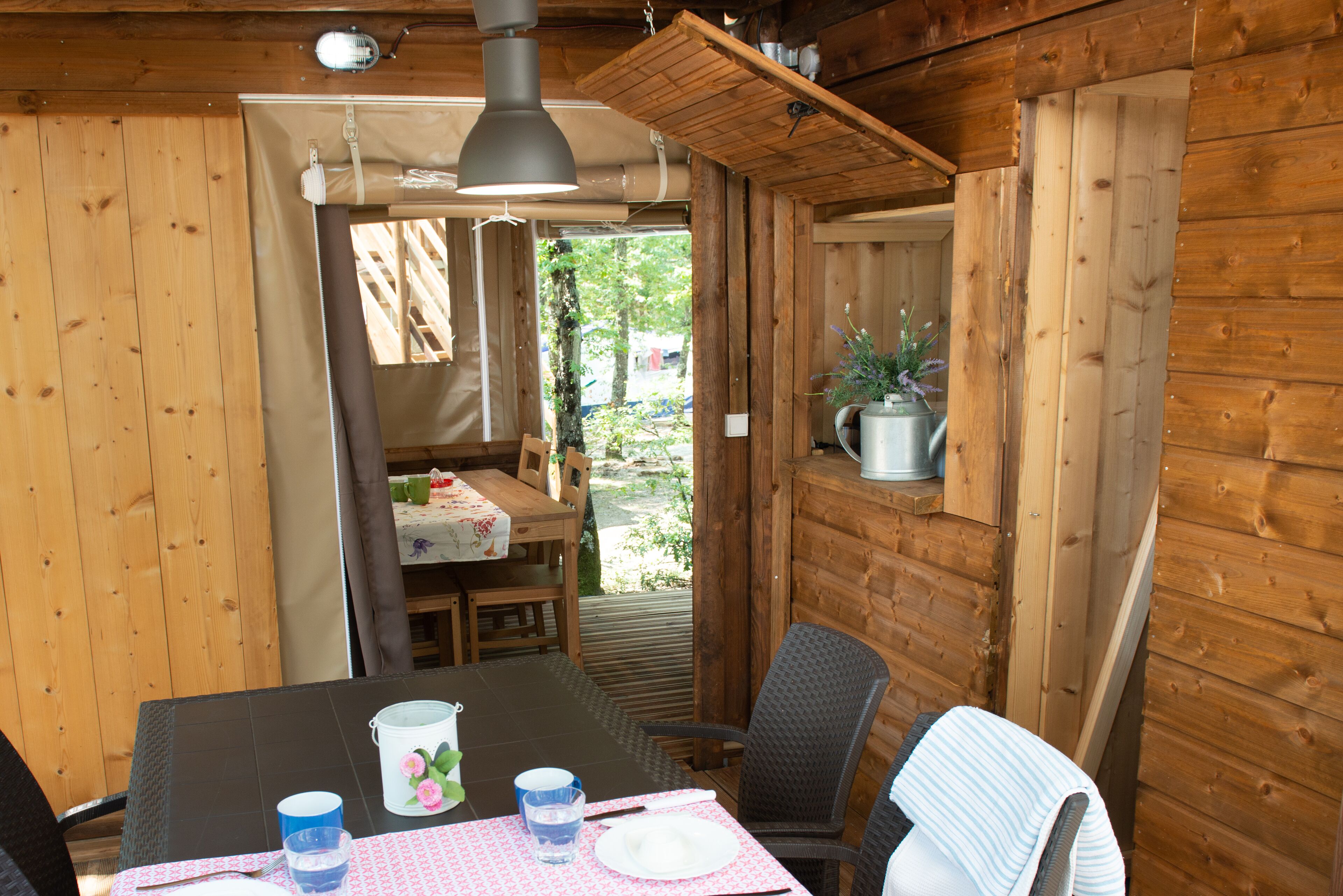 A wooden cabin interior with a dining table, chairs, and a hanging light fixture.