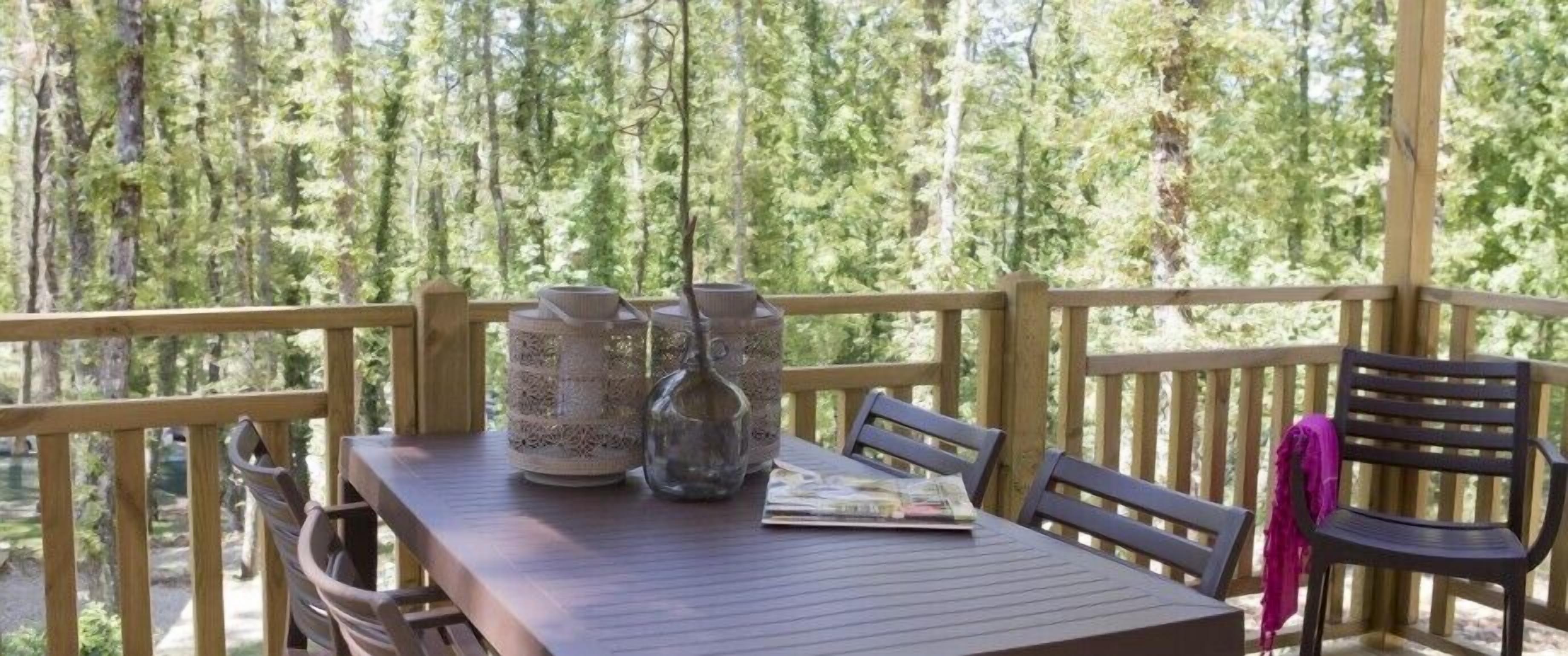 A wooden deck with a table and chairs, surrounded by trees.