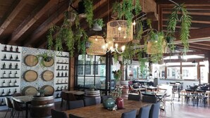 A restaurant interior with wooden beams, hanging plants, and a variety of seating arrangements.