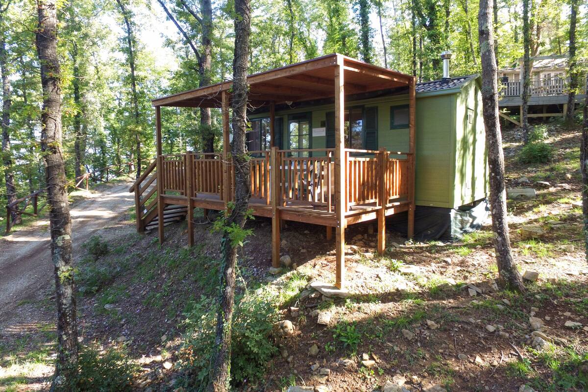 Een houten hutje met een veranda, omringd door bomen.