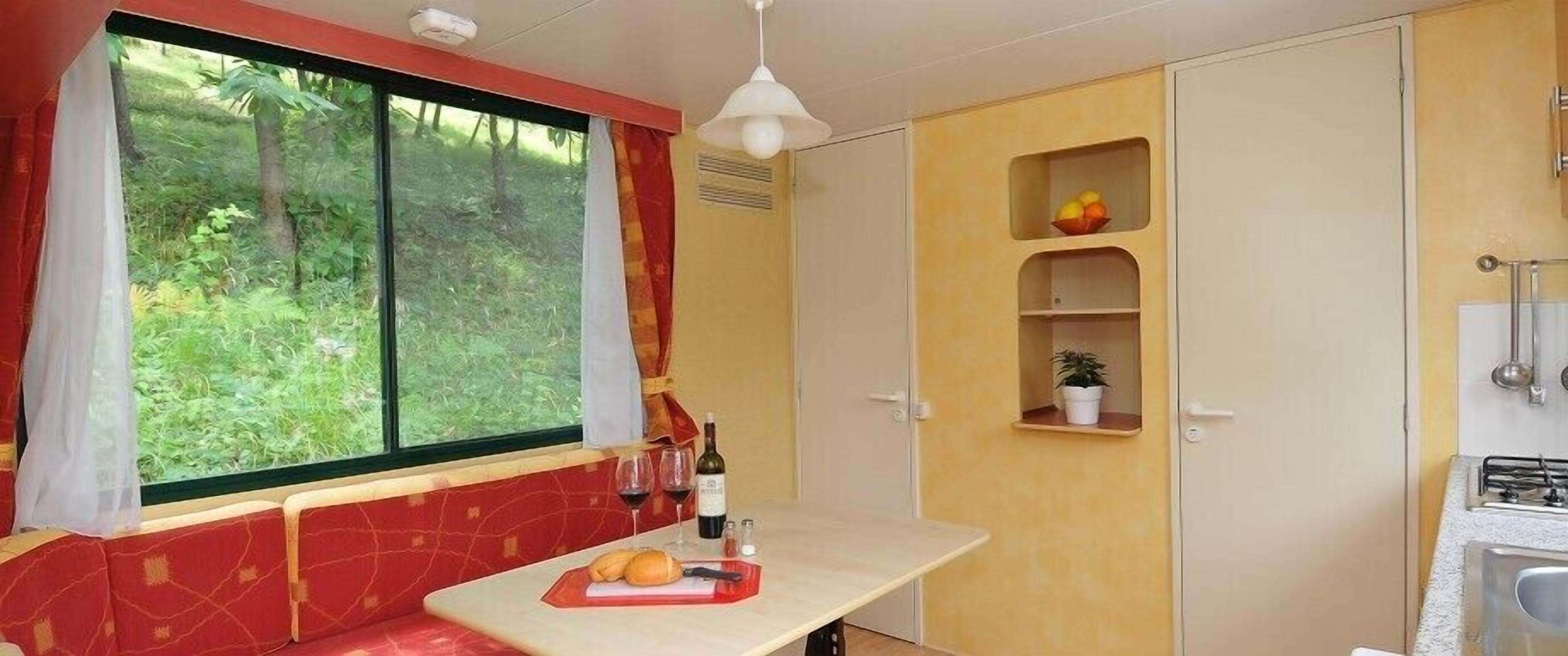 Una cocina compacta con comedor, una ventana con cortinas y un estante con frutas y una planta.