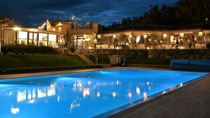A swimming pool with a stone wall and a building with outdoor seating and string lights.