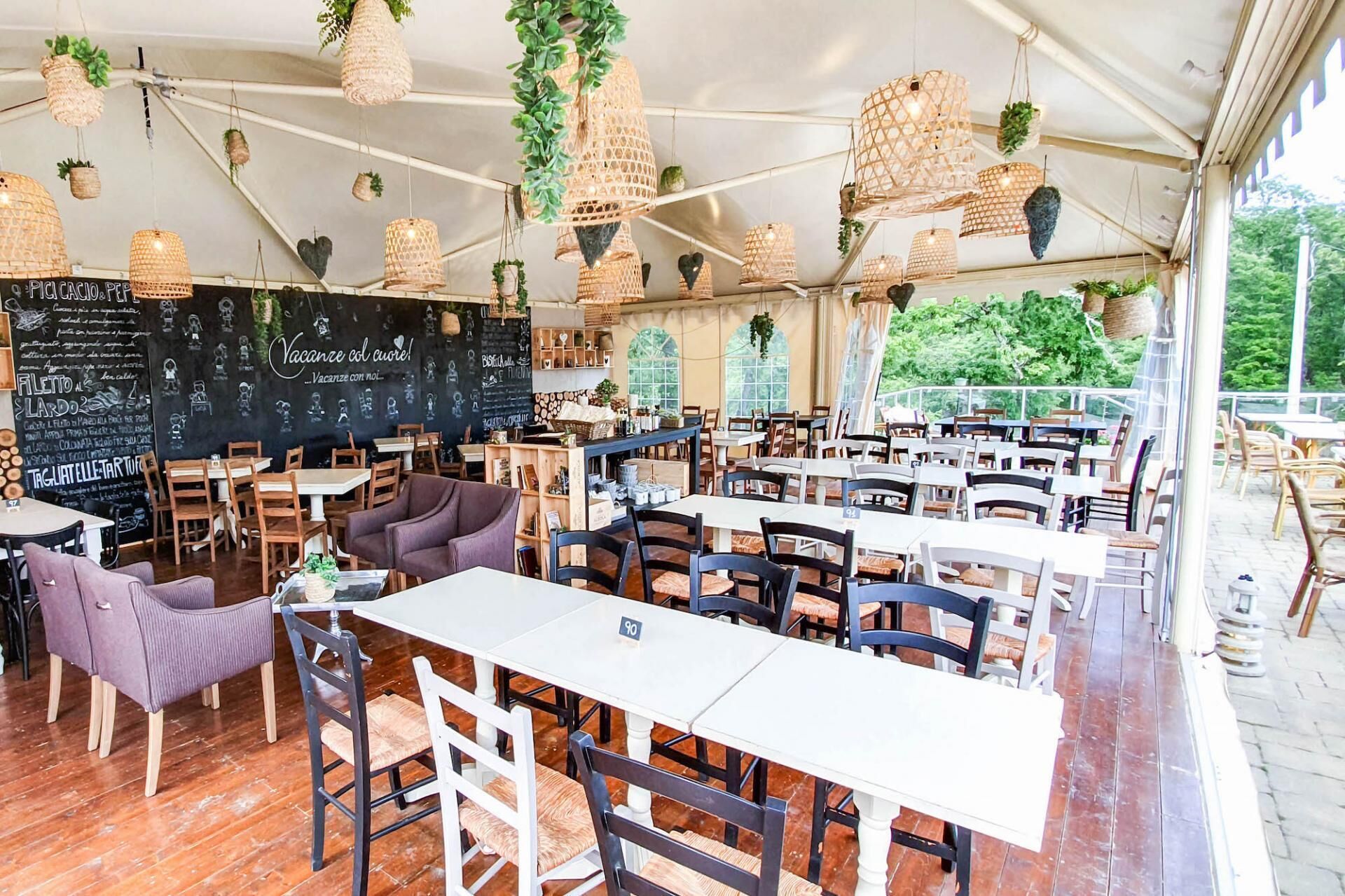 Un comedor interior con mesas y sillas, plantas colgantes y un menú en una pizarra.