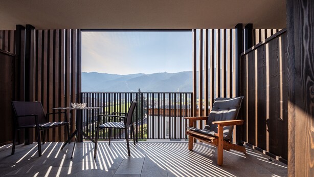 Un balcón con vistas a montañas, que incluye una mesa, sillas y un banco de madera.