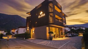 Un edificio moderno con un letrero 'CLARA', una zona de estacionamiento y montañas al fondo.