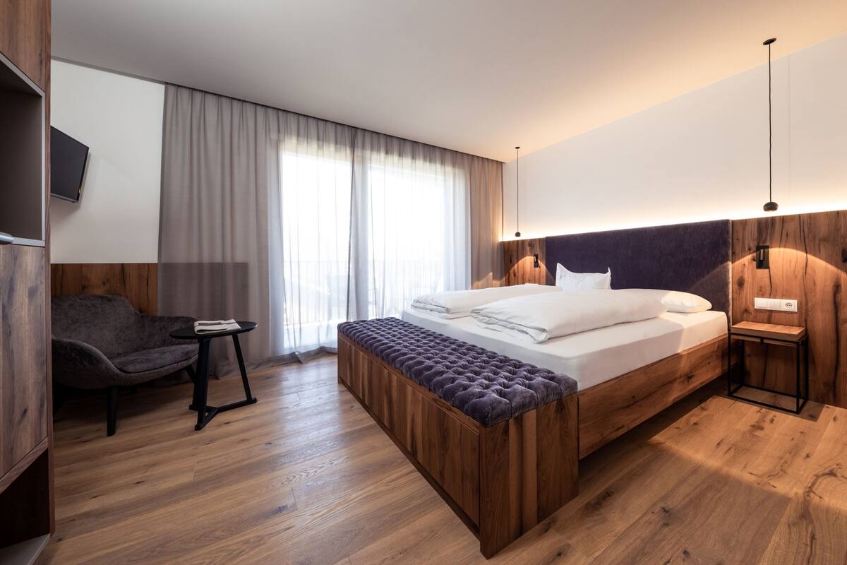 Een moderne hotelkamer met een houten bed, een grijze bank, een klein tafeltje en een aan de muur bevestigde televisie.