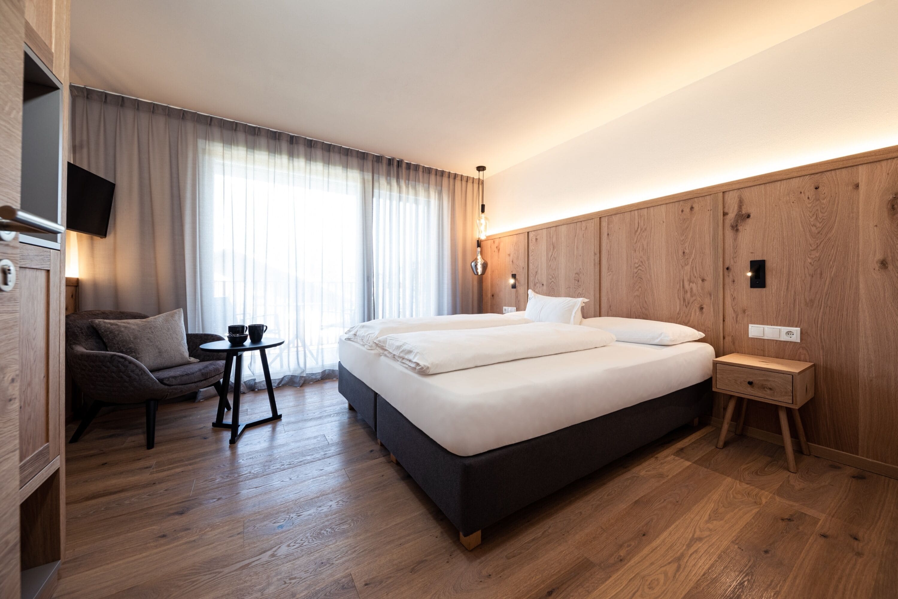 Una habitación de hotel moderna con una cama grande, una mesita, un sofá y un televisor.