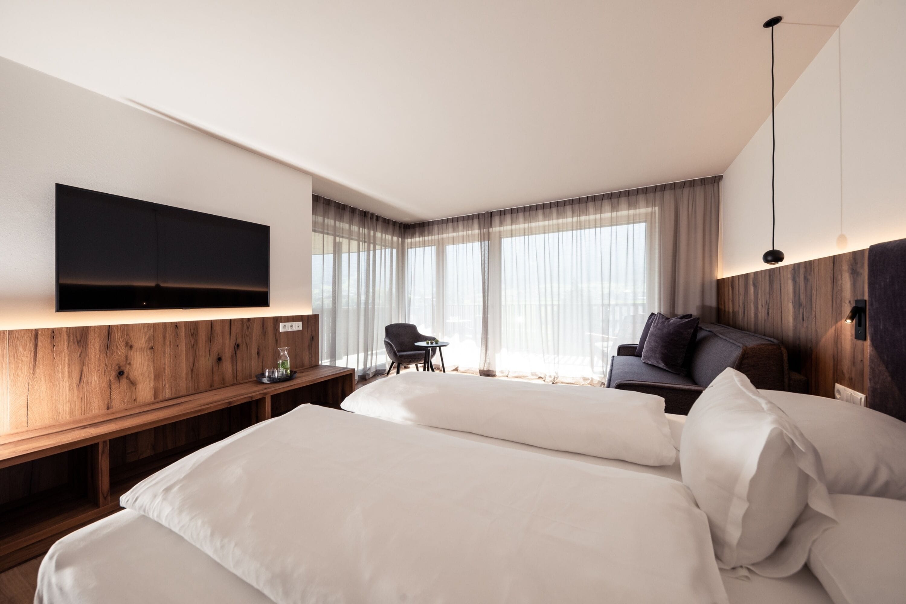 A modern hotel room with a large bed, a desk, a chair, and a TV mounted on the wall.