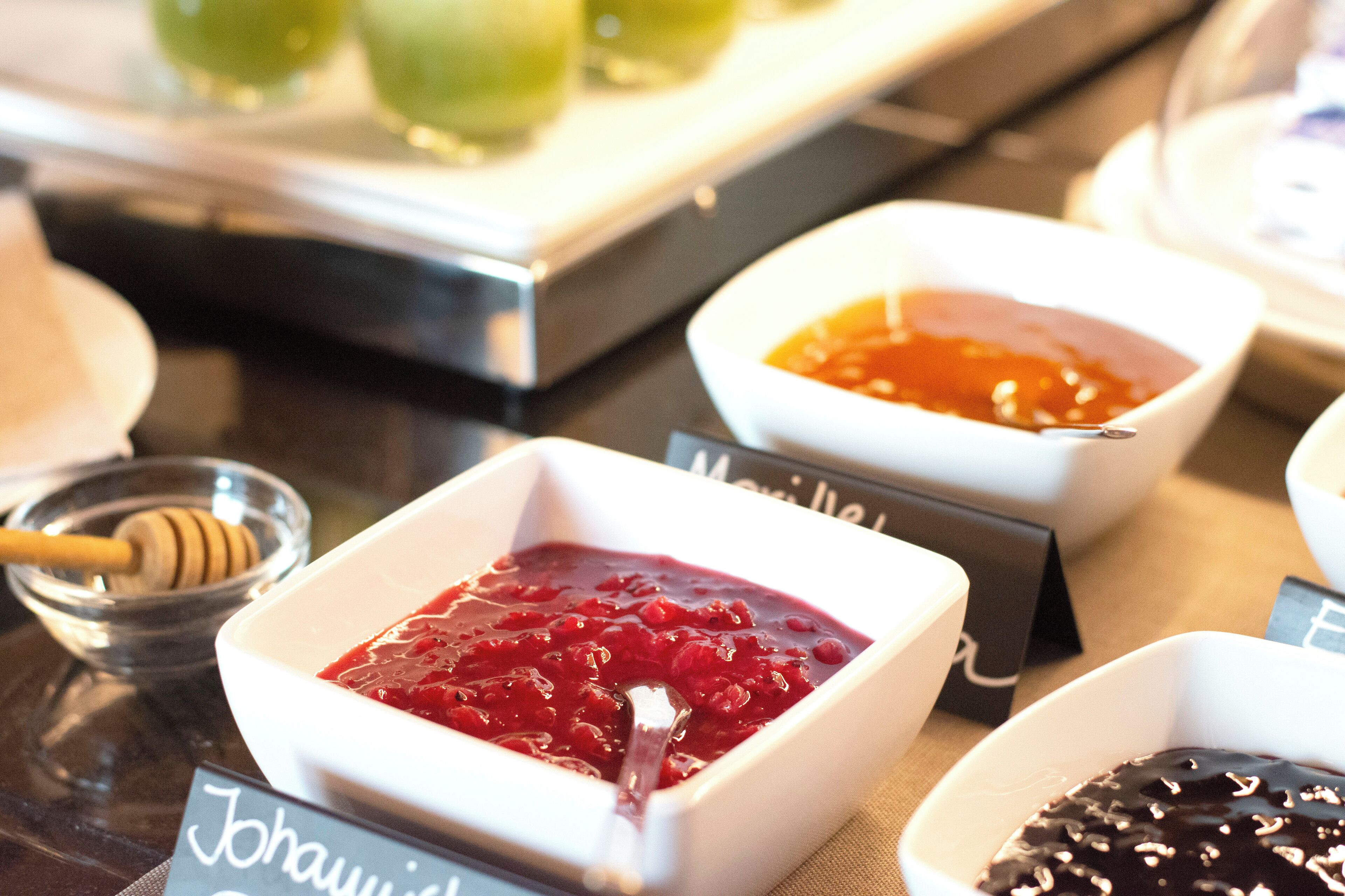 A buffet table with various dishes, including a bowl of red fruit compote and a bowl of dark sauce.