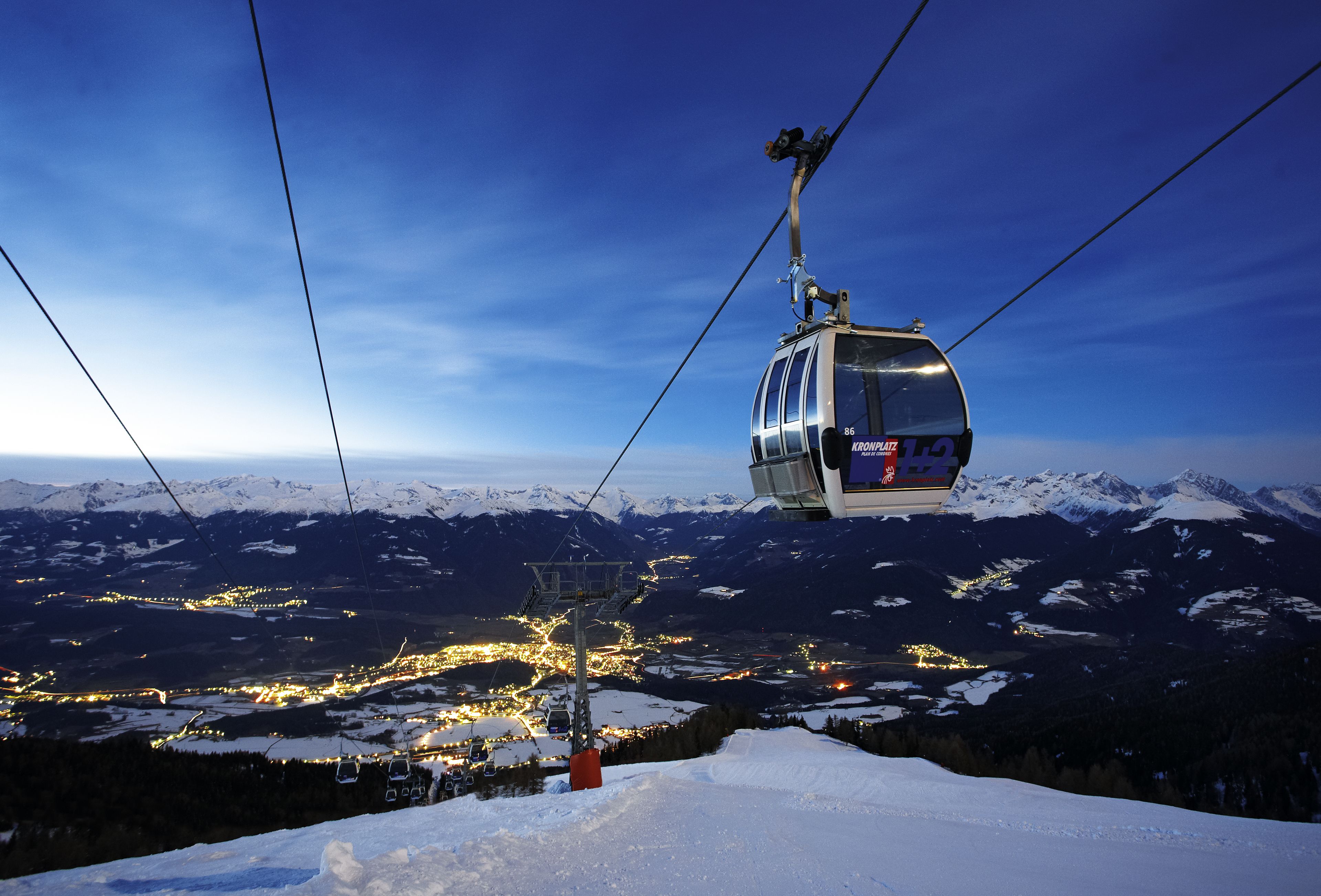 Un teleférico asciende un monte nevado con un pueblo en la parte inferior.