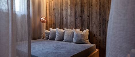 Quarto moderno com parede de madeira, cama com roupa de cama cinza e luminária pendente.