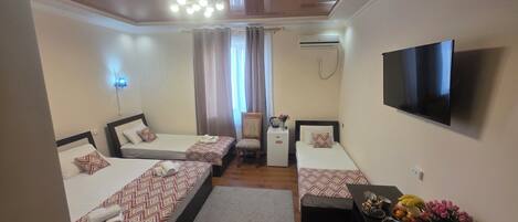 Habitación de hotel con dos camas, televisión, refrigerador pequeño y escritorio con un jarrón de flores.