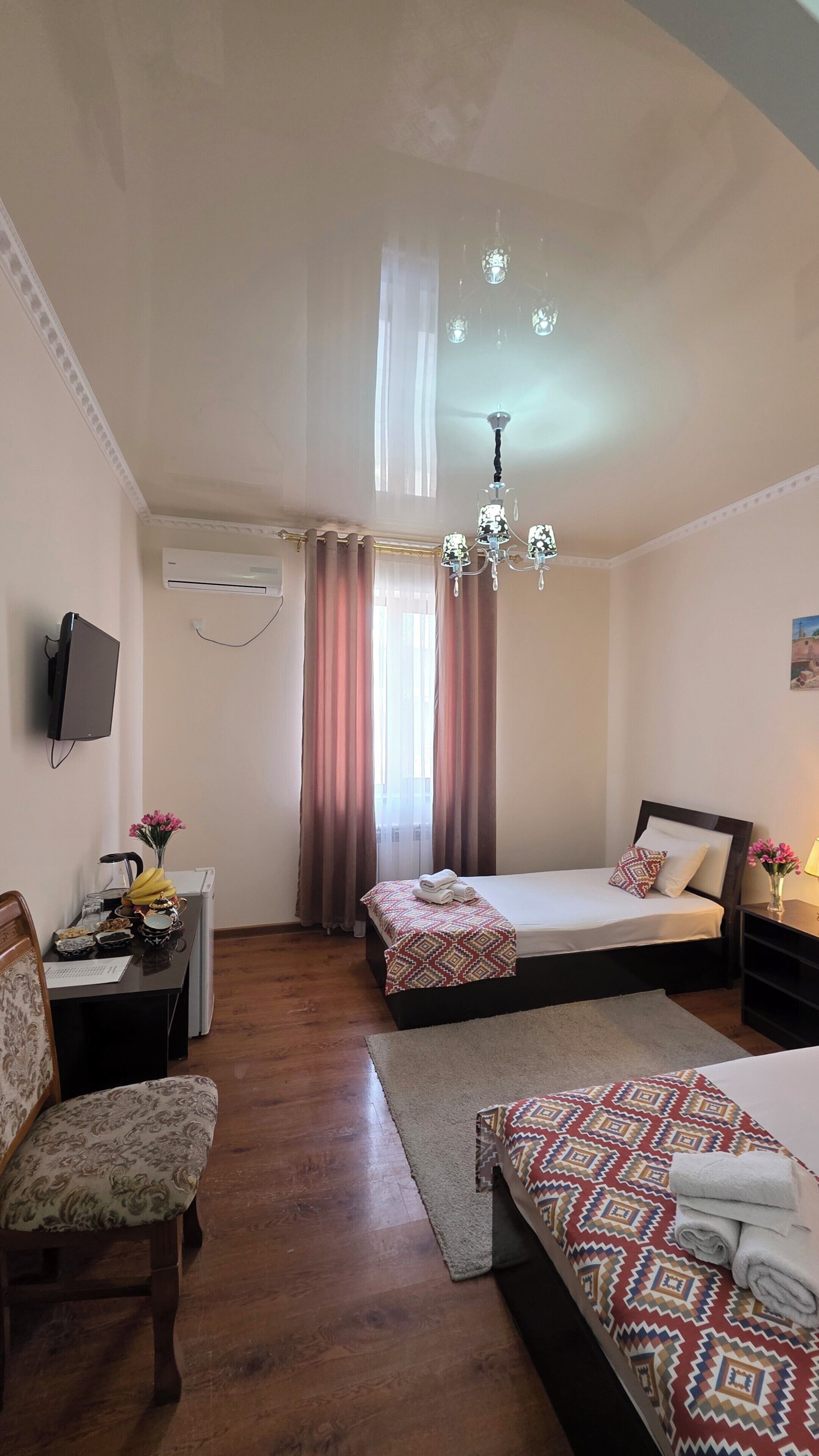A hotel room with a bed, a desk, a chair, a TV, and a chandelier.