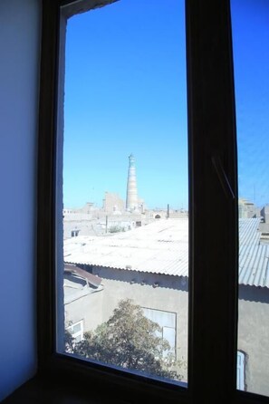 A window view of a building with a tall tower, possibly a lighthouse, and a clear blue sky. - Euro Asia Hotel in Ichan Kala (Khiva)