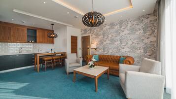 A modern living room with a sofa, armchair, and coffee table. There is a kitchen area with wooden cabinets and a dining table.