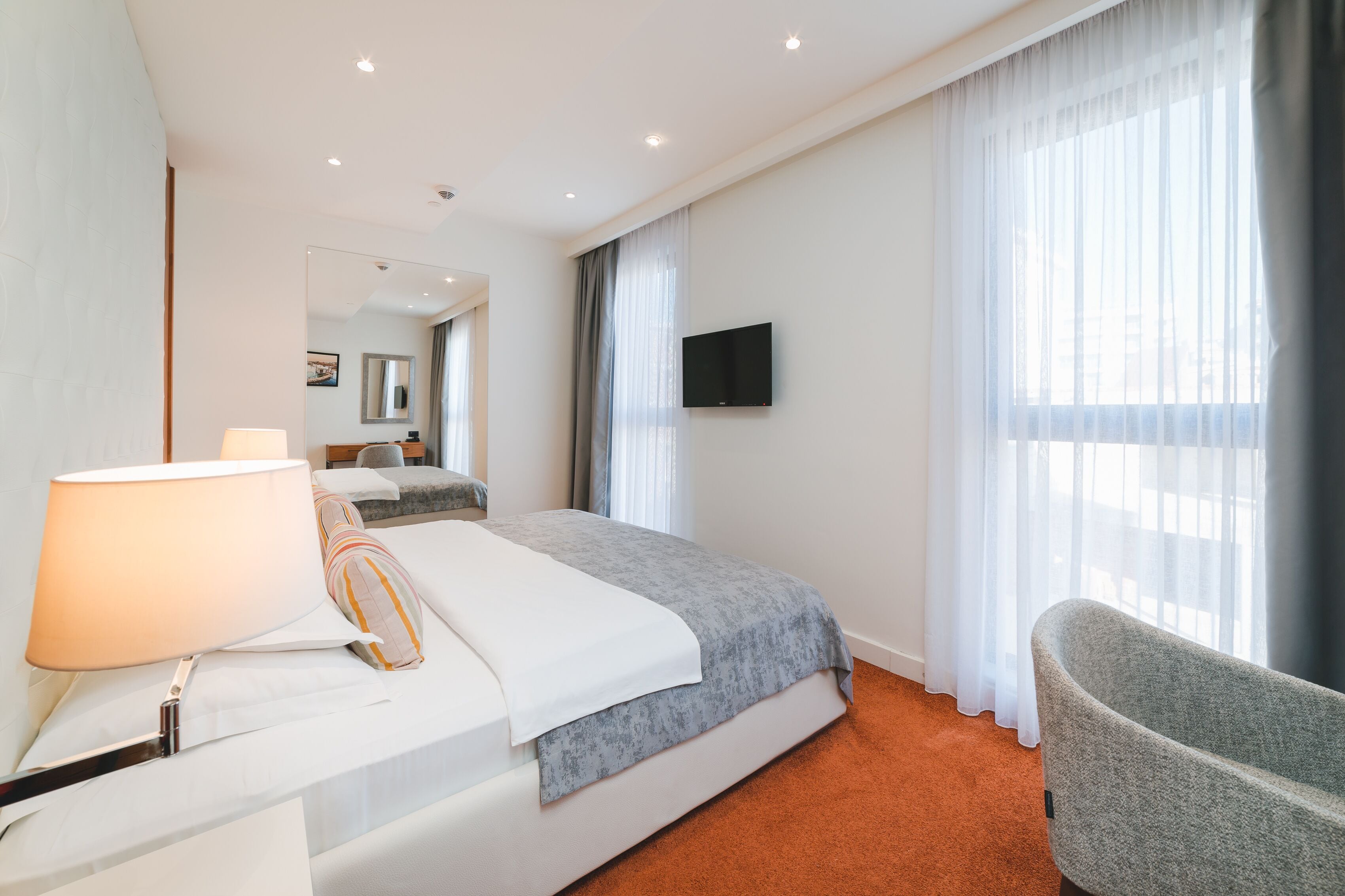 A hotel room with a bed, a chair, a TV, and a window with curtains.