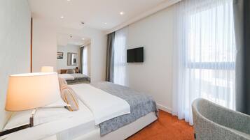 A hotel room with a bed, a chair, a TV, and a window with curtains.