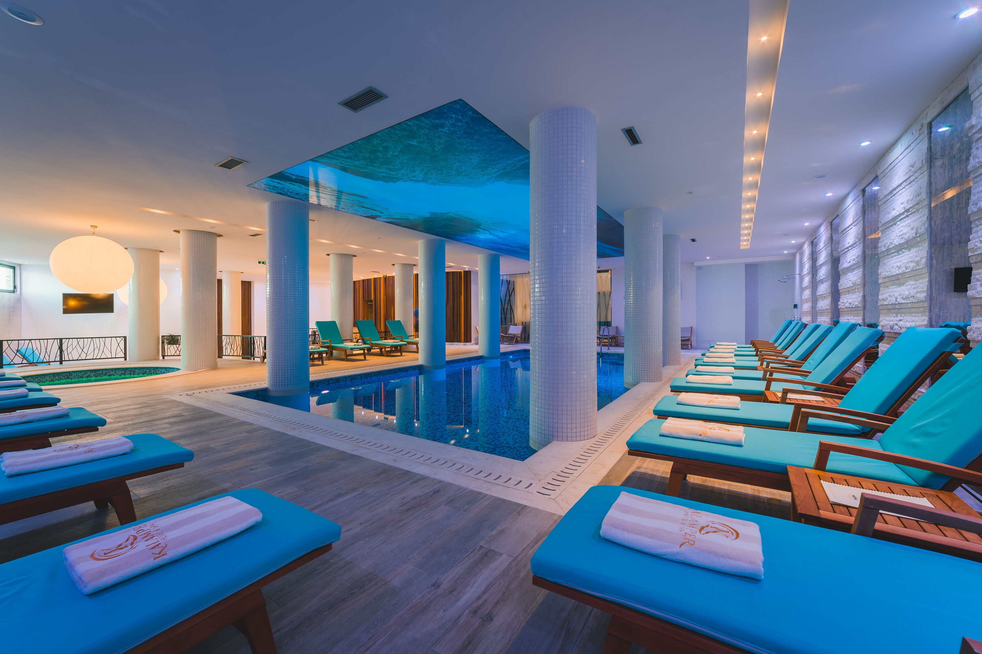 Un área de piscina interior moderna con sillas de descanso azules y una piscina grande.