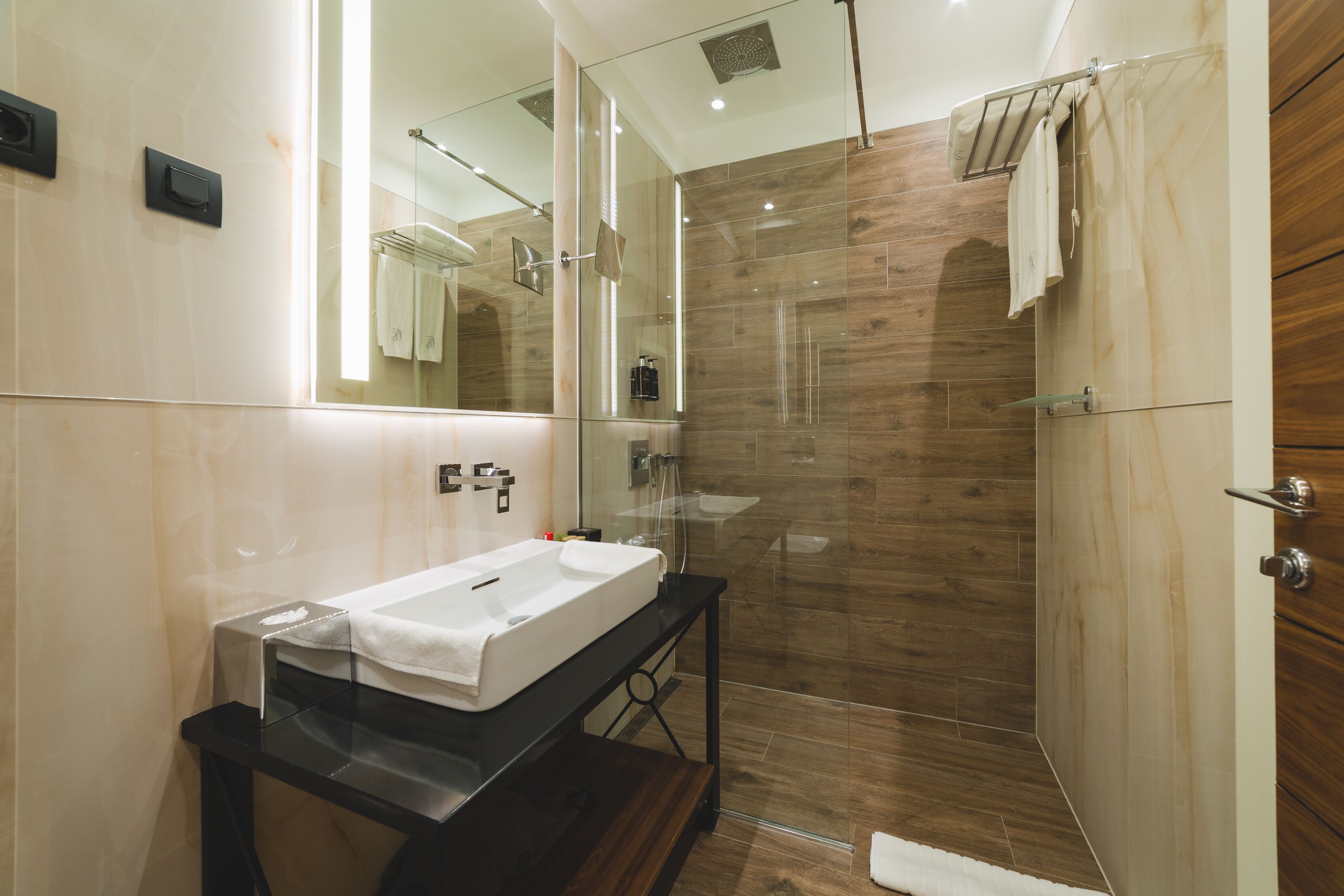 Un baño moderno con ducha envuelta en vidrio, un espejo grande y un mueble de tocador de madera.