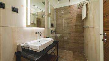 Un baño moderno con ducha envuelta en vidrio, un espejo grande y un mueble de tocador de madera.