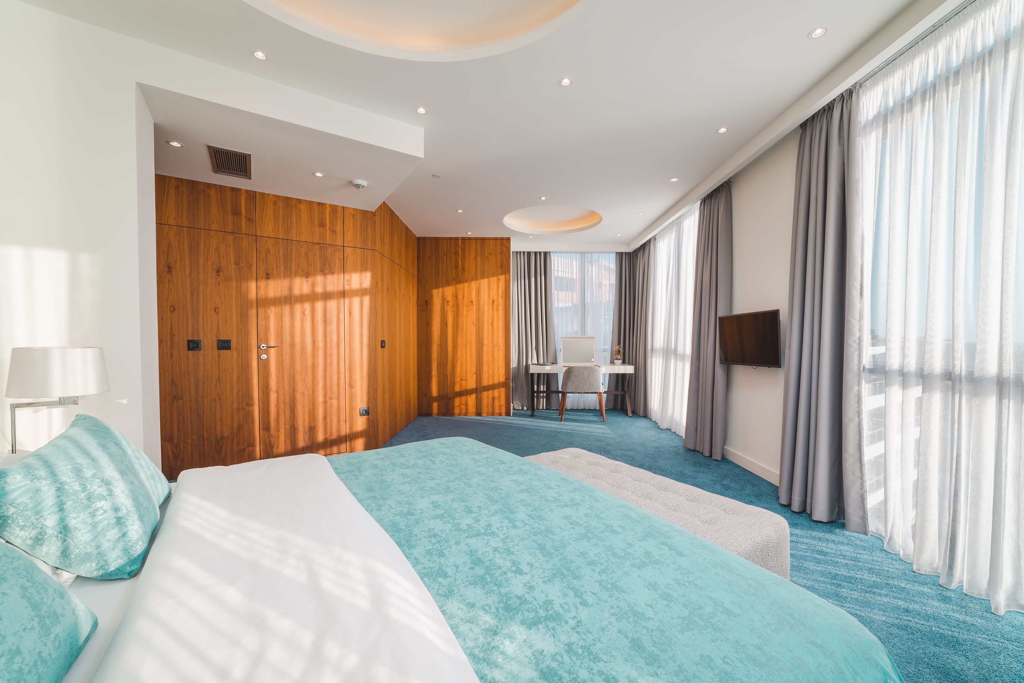 A modern hotel room with a large bed, a desk, and a TV.