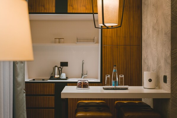 A compact kitchen with a white countertop, wooden cabinets, a coffee maker, a kettle, and a water dispenser. - Kalamper Hotel & Spa (Bar)