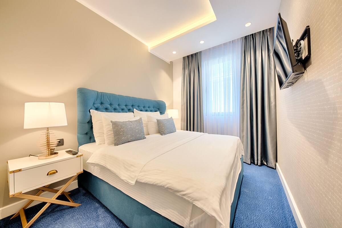 Una habitación de hotel moderna con una cama grande, una mesita de noche con lámpara y un televisor de pantalla plana en la pared.