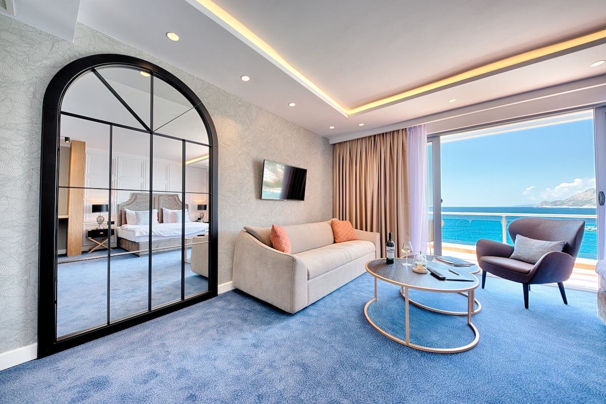 Habitación de hotel moderna con un espejo arqueado grande, un sofá, una mesa de centro y vistas al mar.
