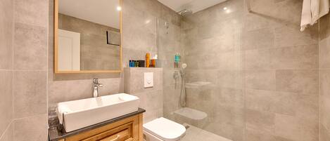 A modern bathroom with a large mirror, a white sink, a wooden vanity, a toilet, and a glass-enclosed shower area.