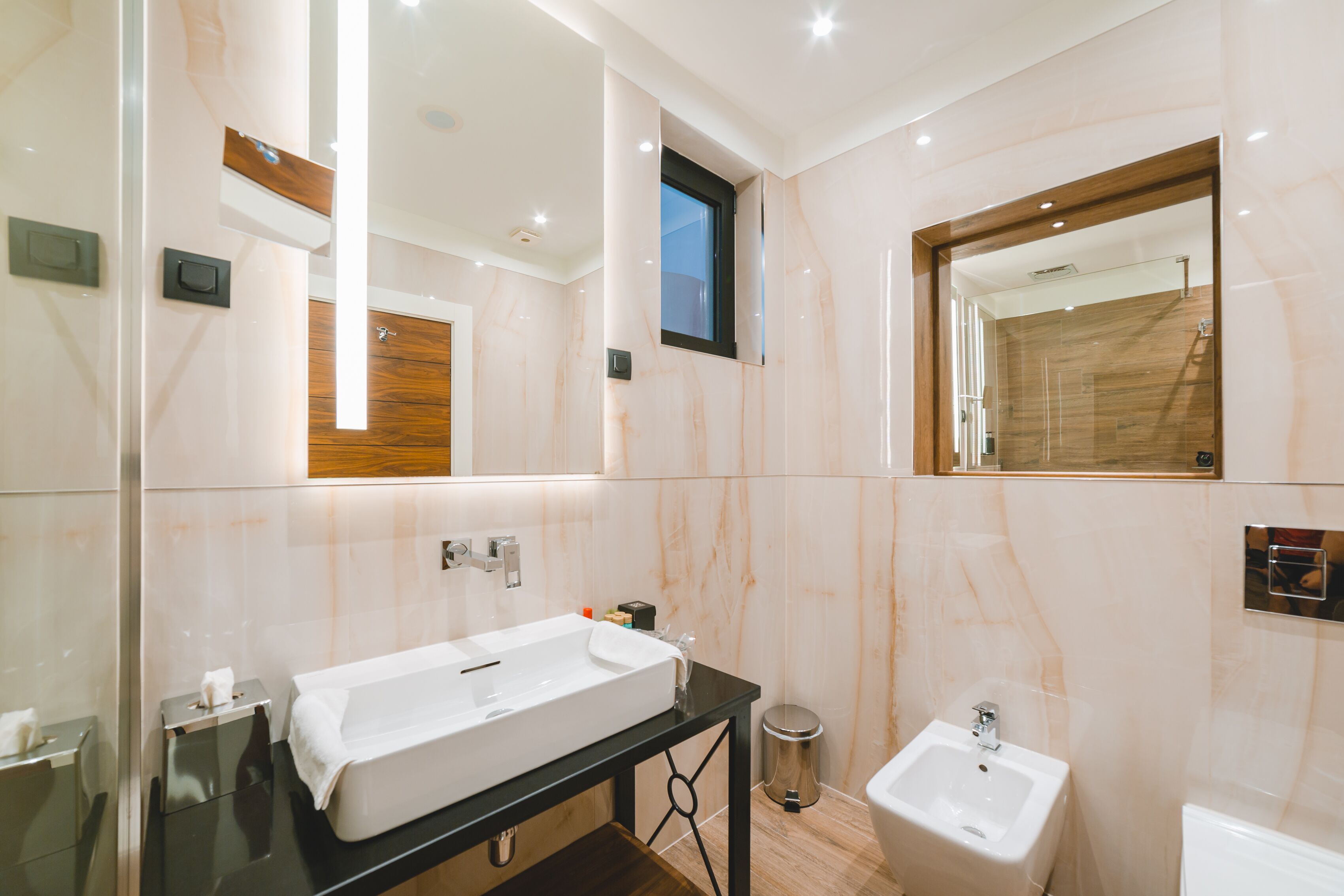 A modern bathroom with a large mirror, a sink, a bidet, and a vanity with a mirror.