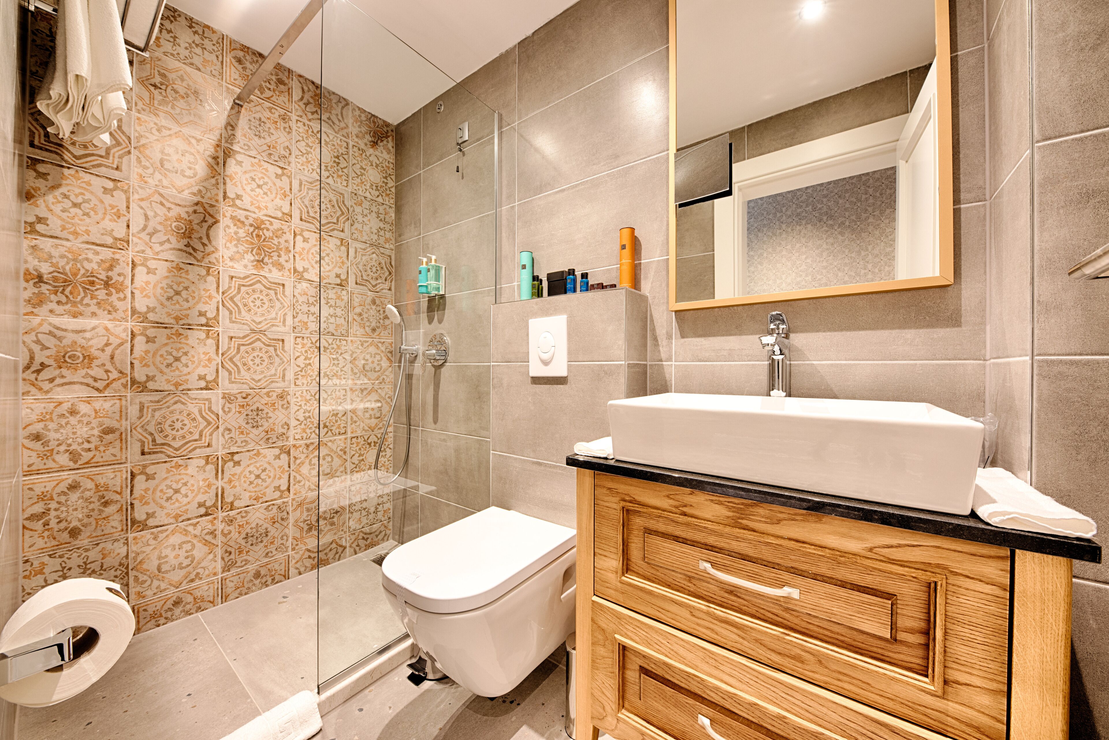 Et moderne badeværelse med bruser, toilet, vaskebord og et stort spejl.