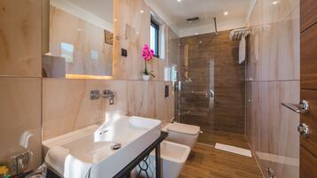A modern bathroom with a large mirror, a white sink, a glass shower enclosure, and wooden flooring.
